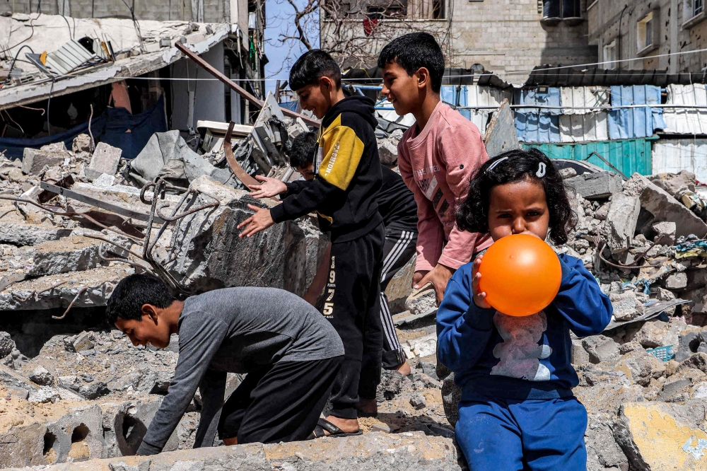 A girl blows a balloon as behind her boys search through the rubble of a destroyed building in Rafah in the southern Gaza Strip on April 5, 2024 amid the ongoing conflict in the Palestinian territory between Israel and Hamas. — AFP pic
