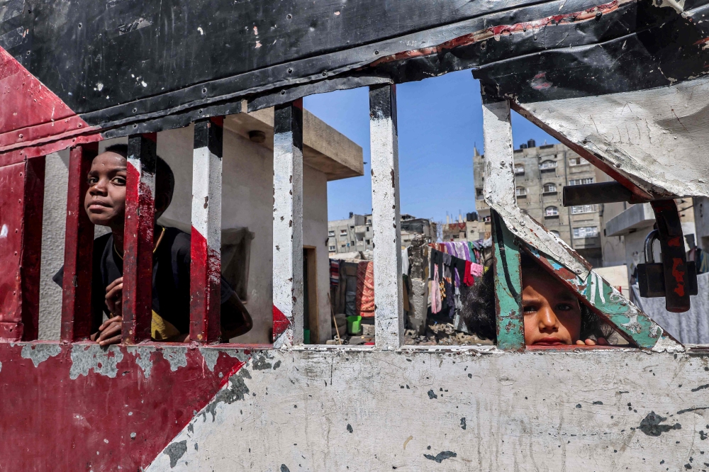 Children look on from behind the a gate of an enclosed area, painted in the colours of the Palestinian flag, in Rafah in the southern Gaza Strip on April 5, 2024 amid the ongoing conflict between Israel and Hamas. — AFP pic