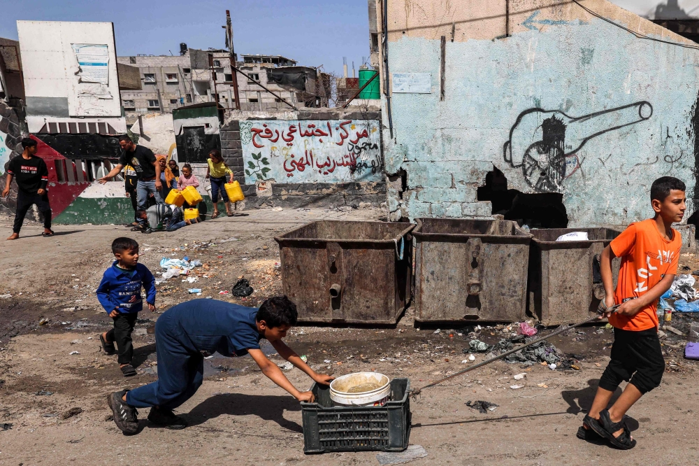 Boys transport a bucket filled with water in Rafah in the southern Gaza Strip on April 5, 2024 amid the ongoing conflict in the Palestinian territory between Israel and Hamas. — AFP pic