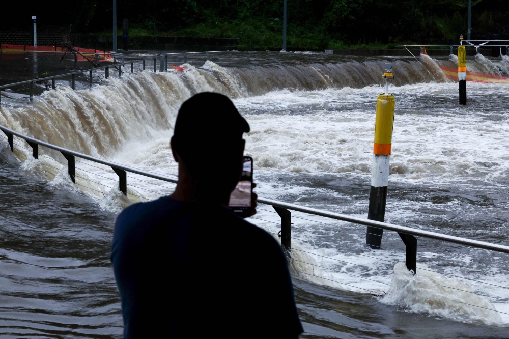 File photo of a man taking pictures of the overflowing Parramatta river at the ferry wharf in Sydney on April 5, 2024, after heavy rain lashed eastern Australia, causing flash flooding and a string of emergency warnings up and down the Pacific coast. — AFP pic