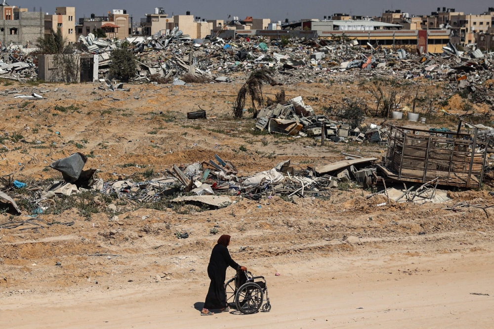 A Palestinian elderly woman pushes a wheelchair past rubble in Khan Yunis on April 7, 2024 after Israel pulled troops out of the southern Gaza Strip, six months into the devastating war following the October 7 attacks. — AFP pic