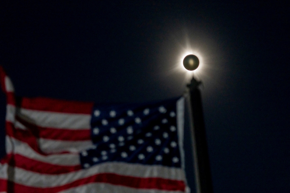 A total solar eclipse is seen beside a waving American flag in Houlton, Maine April 8, 2024.  — Picture by Jasper Colt/USA Today Network via Reuters