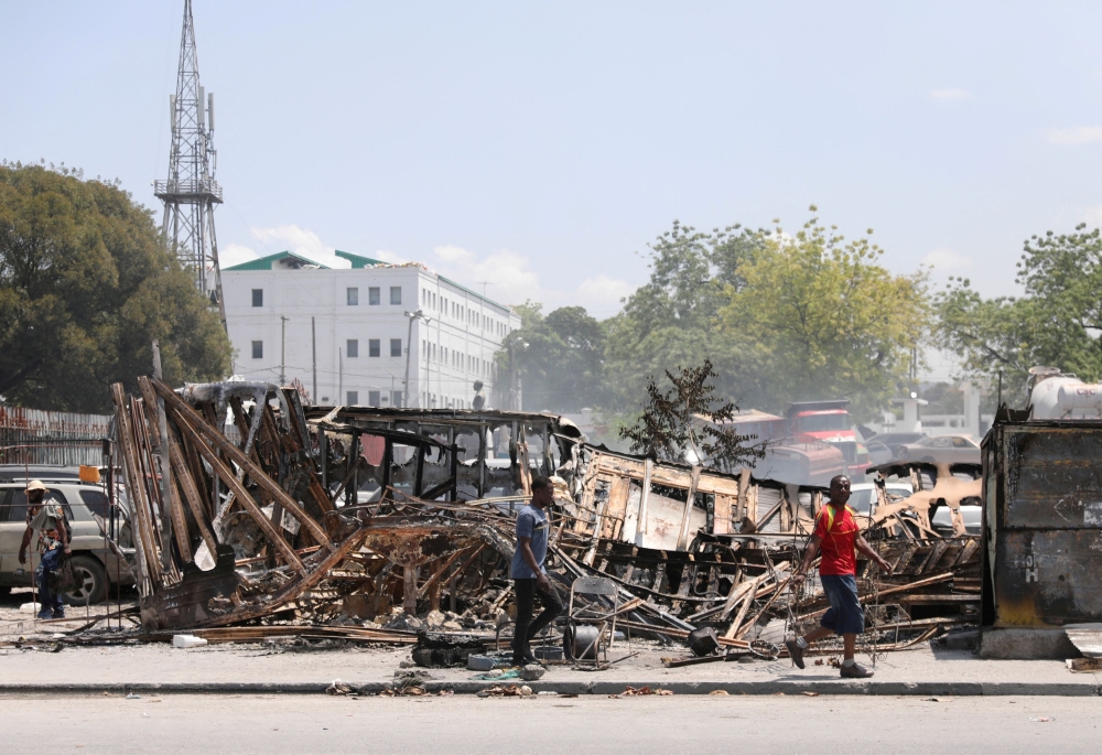 People walk past remains of vehicles near the presidential palace, after they were set on fire by gangs, as violence spreads and armed gangs expand their control over the capital, in Port-au-Prince, Haiti March 25, 2024. — Reuters pic