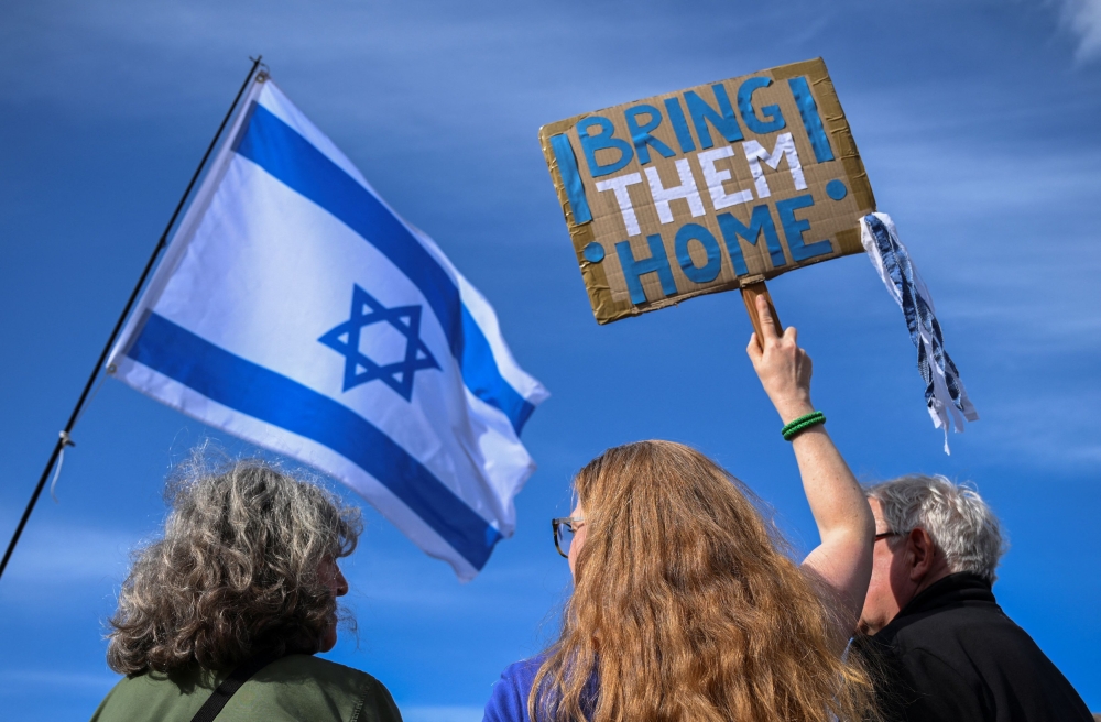 People holding an Israeli flag and a placard calling for bringing October 7 attack hostages home, gather for a rally in solidarity with Israel, after Iran launched drones and missiles towards Israel, in Berlin, Germany, April 14, 2024.  — Reuters pic