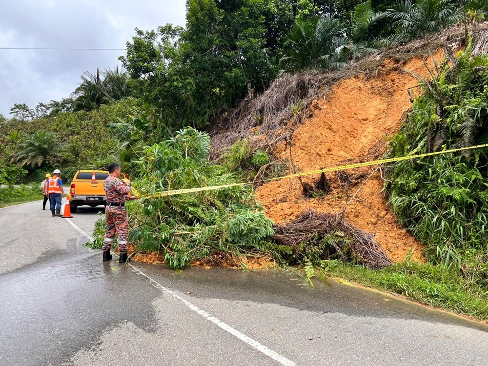 A Bomba personnel puts up safety tape to warn motorists of the landslide at the road leading to Rumah Sumang.