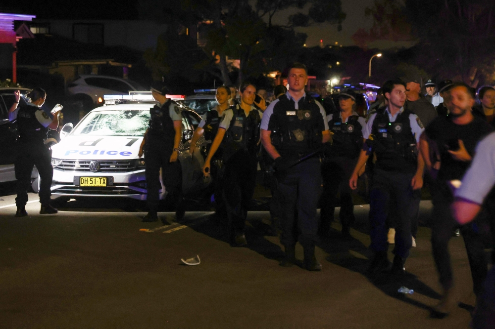 New South Wales police walk past a damaged police car after a mob was pushed back outside the Christ the Good Shepherd Church in Sydney. — AFP pic