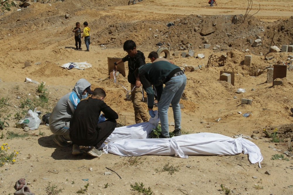 Palestinians cover a body, which was buried in a mass grave, amid the ongoing conflict between Israel and Hamas, in northern Gaza Strip, April 15, 2024. ― Reuters pic