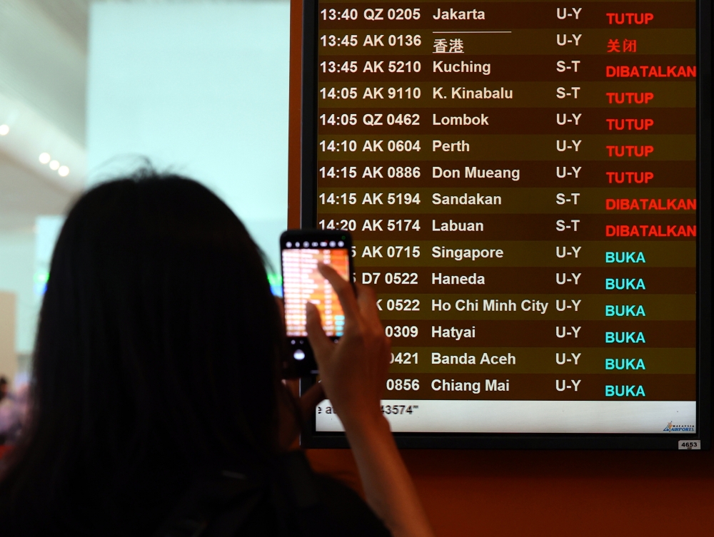 An AirAsia passenger records flight schedules following the cancellation of all flights from Kuala Lumpur International Airport (KLIA) Terminal 2 to Sabah, Sarawak, and Brunei until 8am tomorrow, April 18, 2024. — Bernama pic 