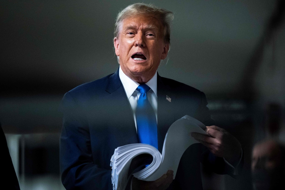 Former US president and Republican presidential candidate Donald Trump holds news clippings as he speaks to the press after the third day of his trial for allegedly covering up hush money payments linked to extramarital affairs at Manhattan Criminal Court in New York on April 18, 2024.  — AFP pic