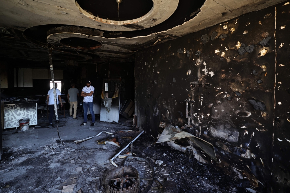 Palestinians stand amid the damage caused by fire, in the aftermath of an Israeli settler attack on the occupied West Bank village of Duma April 17, 2024. — AFP pic
