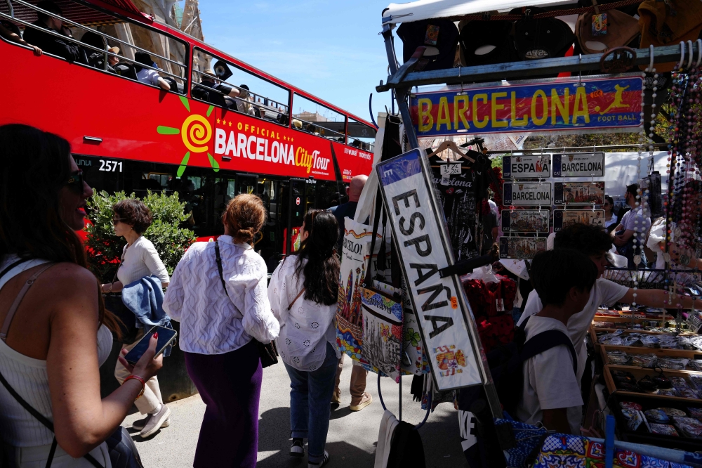 File photo of tourists walking past a souvenir shop and a tourist bus next to Sagrada Familia basilica in Barcelona on April 13, 2024. ― AFP pic