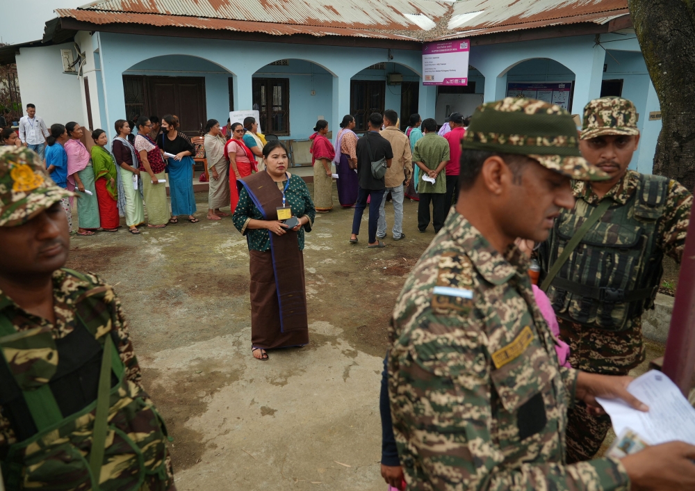 Voters queue as they wait to cast their votes next to security force personnel outside a polling station in Manipur. — Reuters pic