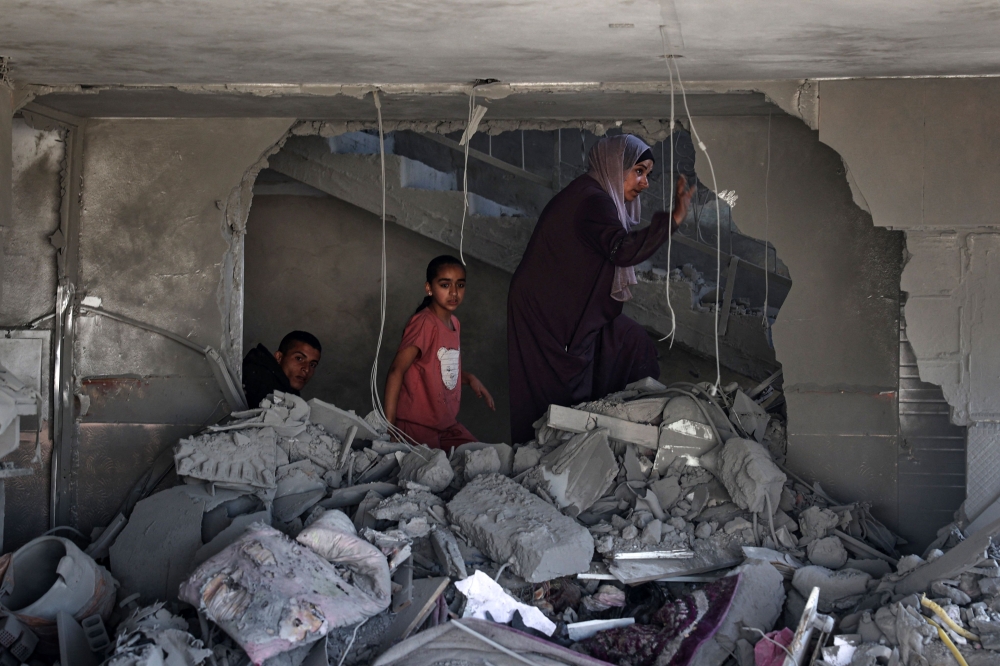 A Palestinian woman and children check the rubble of a building hit by overnight Israeli bombing in Rafah. — AFP pic
