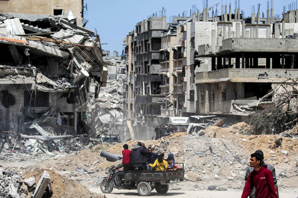 People ride in the back of a three-wheel cargo vehicle moving past destroyed buildings in Khan Yunis in the southern Gaza Strip on April 22, 2024 amid the ongoing conflict in the Palestinian territory between Israel and Hamas. — AFP pic