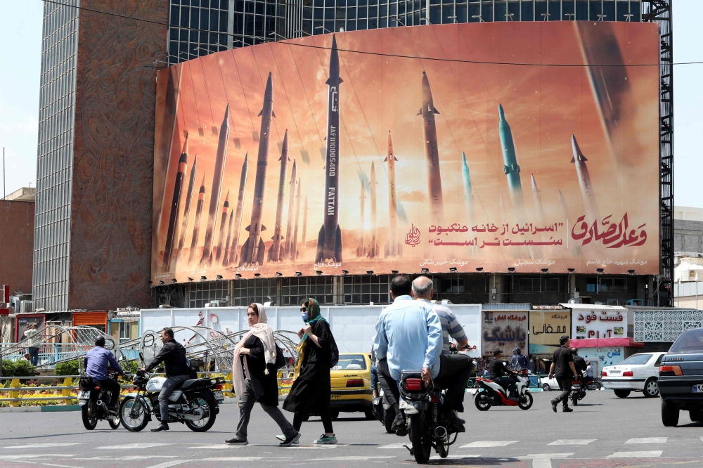 Motorists drive their vehicles past a billboard depicting Iranian missiles in Tehran on April 20, 2024, a day after Iran's state media reported explosions in the central province of Isfahan. — AFP pic