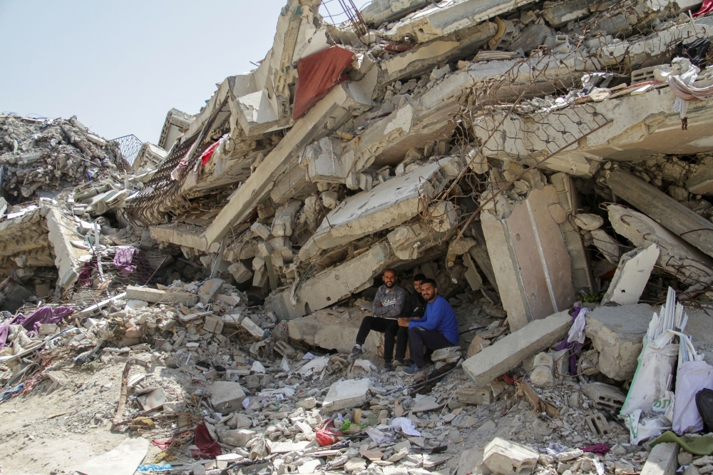 Palestinians sit at the rubble of a residential building destroyed by Israeli strikes. — Reuters pic