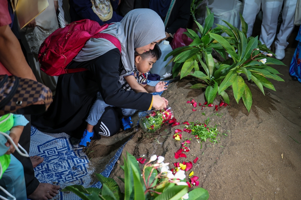 Soffiyah Sa’adon, the wife of the late Commander Muhammad Firdaus Ramli, sprinkles water on the grave of her husband at the Masjid Jamek Sungai Nibong Besar Muslim cemetery, George Town, April 24, 2024. — Bernama pic 