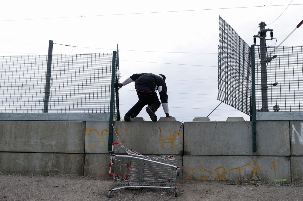 A migrant climbs a wall in a camp in Grande Synthe, after migrants died in an attempt to cross the English Channel April 23, 2024. — Reuters pic  