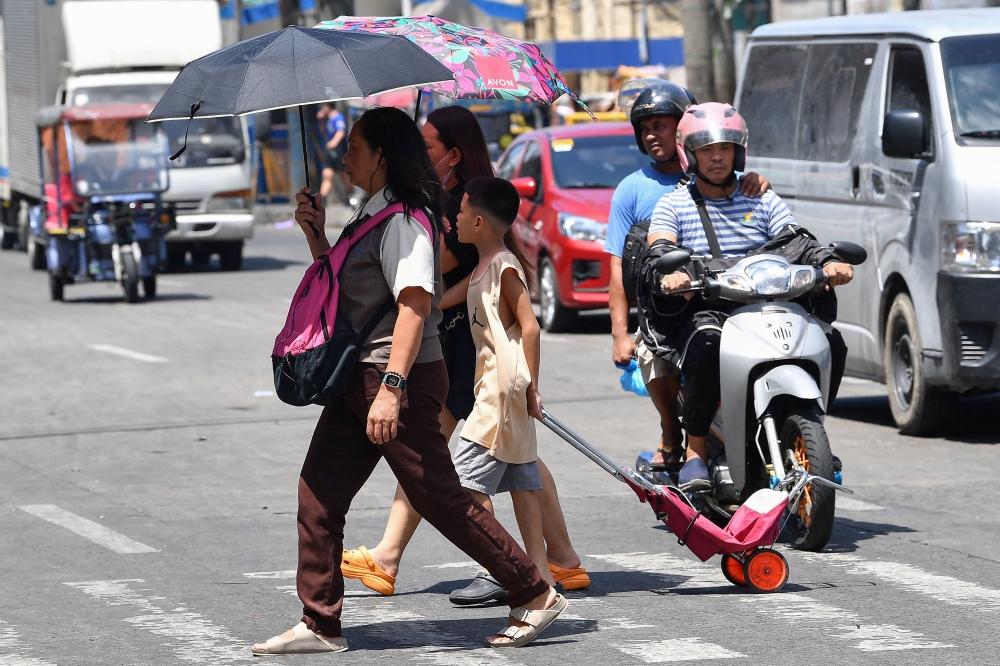 A family holding umbrellas to protect themselves from the sun walk across a street in Manila on April 25, 2024. — AFP pic