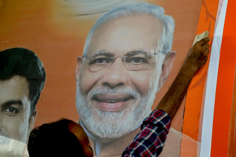 A worker fixes a sticker with a photograph of Bharatiya Janata Party (BJP) leader and Indian Prime Minister Narendra Modi on an election campaign vehicle in Mumbai on April 27, 2024 during the ongoing Indian general election. — AFP pic