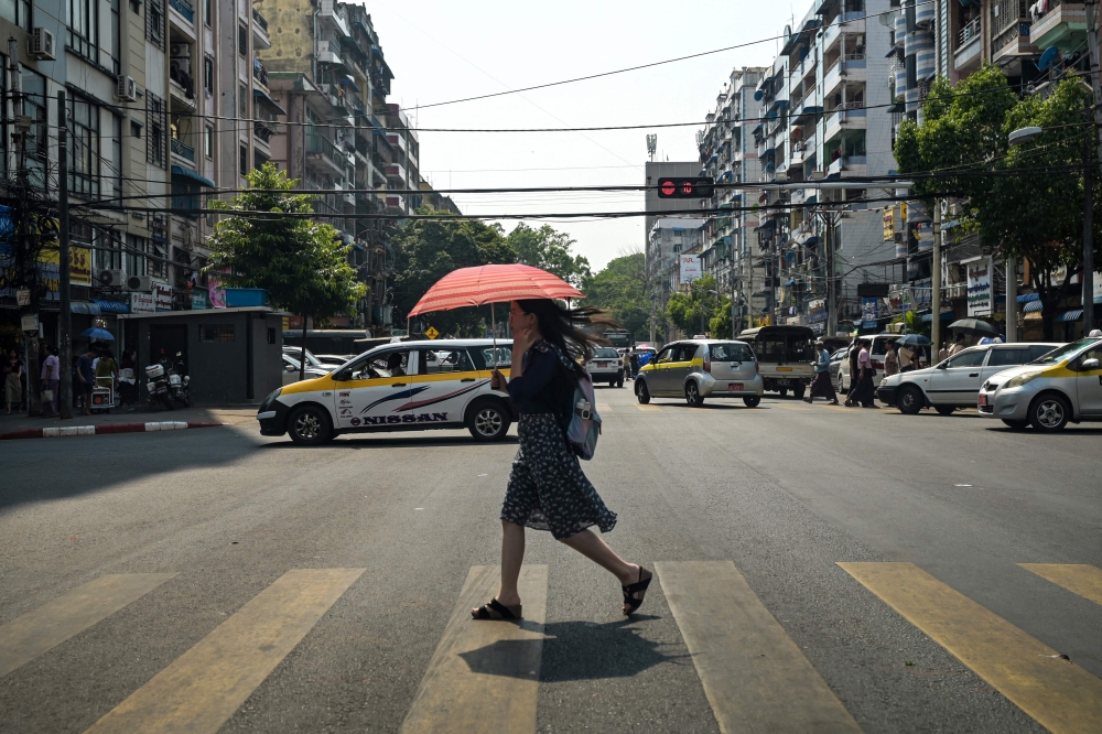 A woman walks under an umbrella to shelter from the sun during a heatwave in Yangon on April 2, 2024. — AFP pic