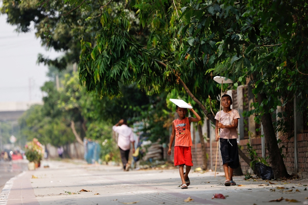 Children hold cork sheets to cover them from the sun while walking along a street during a countrywide heatwave in Dhaka April 28, 2024. — Reuters pic  