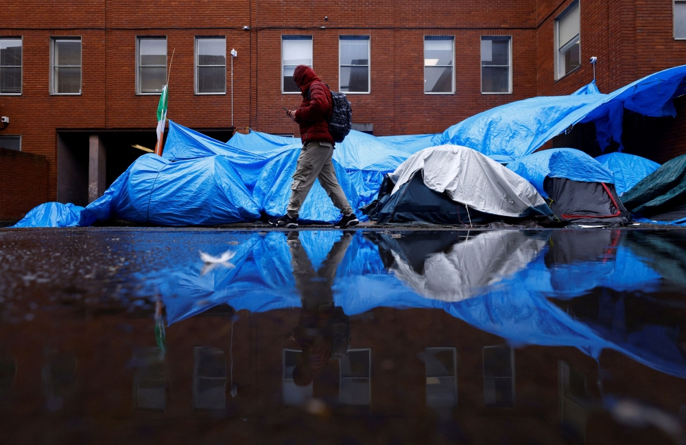 An asylum seeker walks past tents beside the International Protection Office (IPO), where hundreds of migrants in search of accommodation have been sleeping on the streets for several months with more arriving every day, Dublin, Ireland, April 30, 2024. — Reuters pic