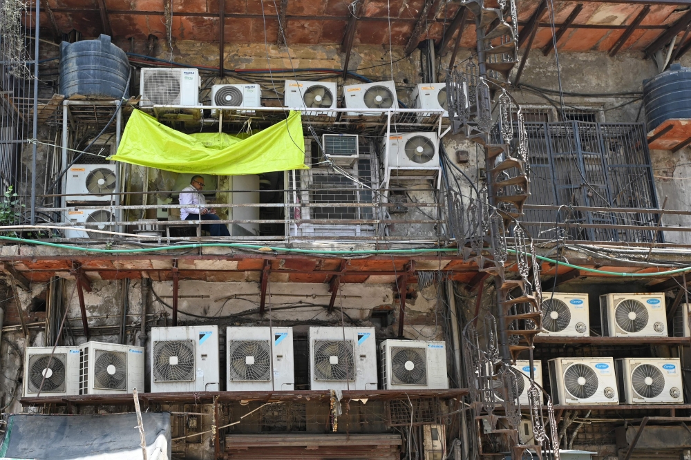 In this photograph taken on May 2, 2024, a man sits in a balcony amid air conditioning units installed on the facade of a building in New Delhi. — AFP pic