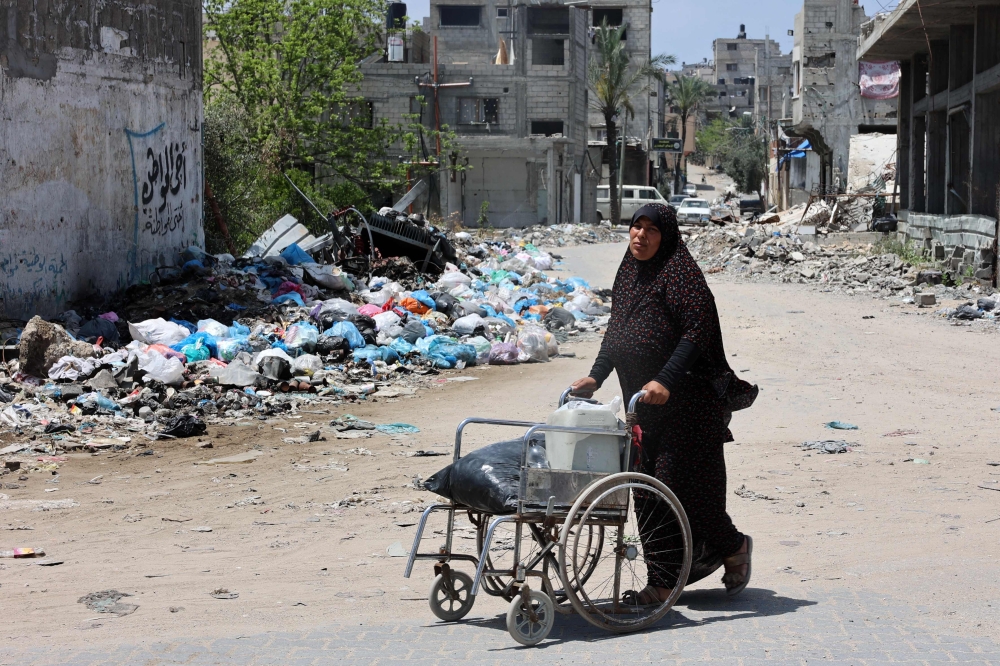 A Palestinian woman pushes a wheelchair packed with food items as she walks past a rubbish dump in Gaza City on May 3, 2024, amid the ongoing conflict between Israel and the militant group Hamas. ― AFP pic