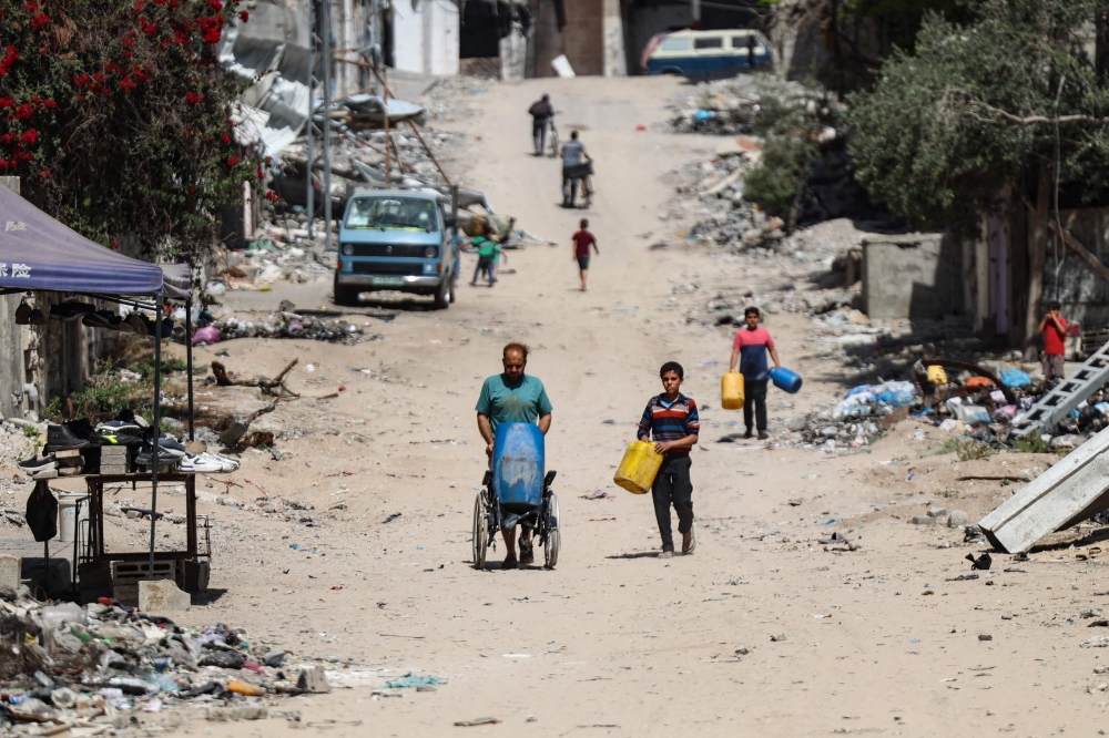 Palestinians carry recipients as they walk toward a water distribution point along a street devastated by Israeli bombardment in Gaza City on May 3, 2024, amid the ongoing conflict between Israel and the militant group Hamas. ― AFP pic