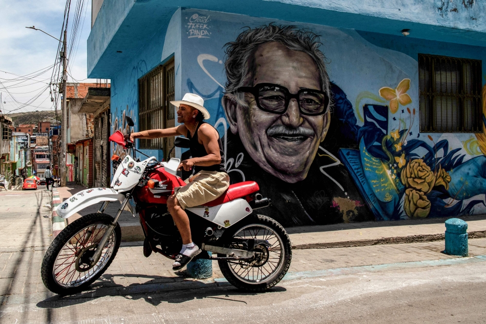 A man riding a motorcycle is pictured in front of graffiti of Colombian writer Gabriel Garcia Marquez during a tour of the Ciudad Bolivar neighbourhood in Bogota April 14, 2024. — AFP pic