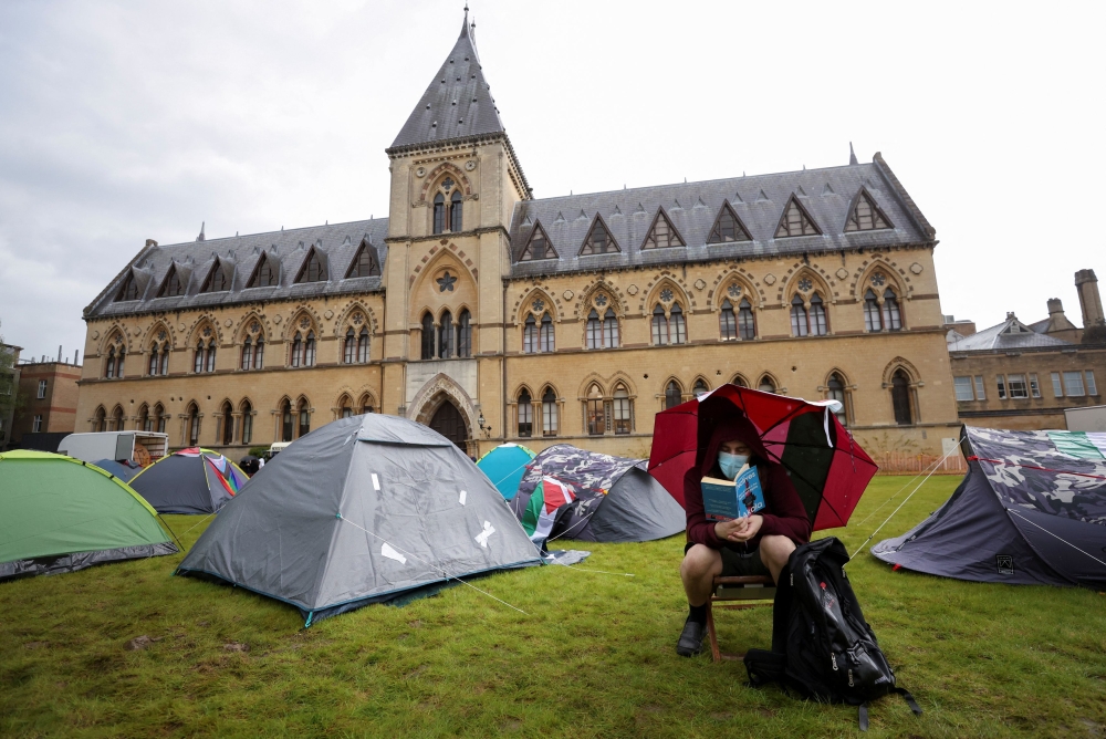 A local activist reads near tents at Oxford University, outside Oxford University Museum of Natural History, as students occupy parts of British university campuses to protest in support of Palestinians in Gaza, amidst the ongoing conflict between Israel and the Palestinian Islamist group Hamas, in Oxford, Britain, May 6, 2024. — Reuters pic