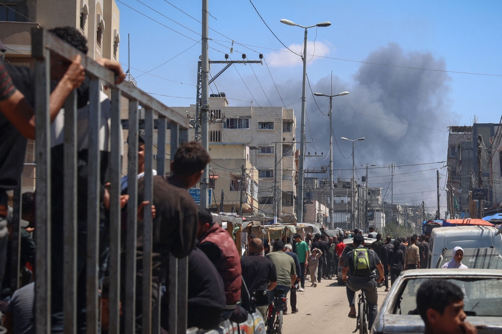 Palestinians crowd a street as smoke billows nearby from Israeli strikes in Rafah in the southern Gaza Strip on May 7, 2024. — AFP pic