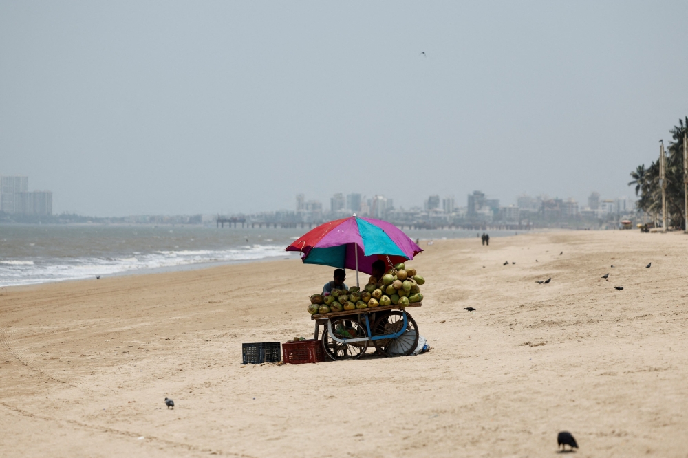 A vendor selling coconut water waits for customers at a beach on a hot day in Mumbai, India. — Reuters pic