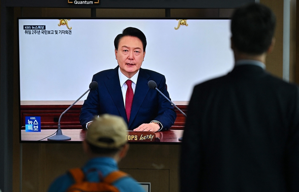 People watch a television news screen broadcasting live footage of South Korean President Yoon Suk-yeol at a press briefing. — AFP pic