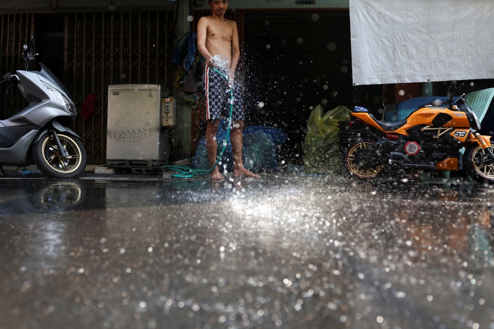 A Thai resident splashes water in front of his home to bring down the temperature. — Reuters pic