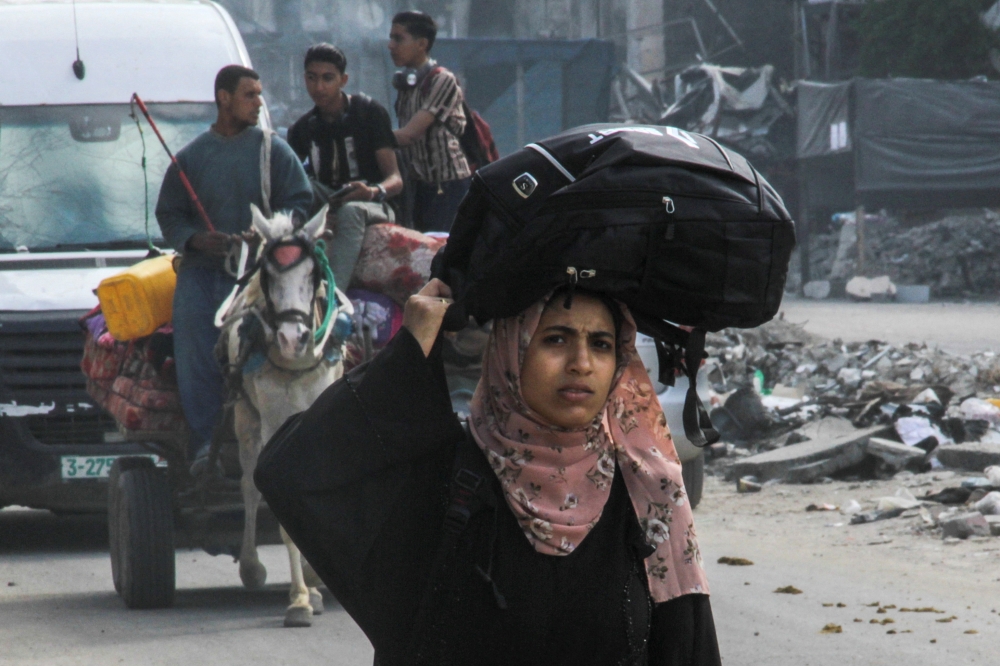 A displaced Palestinian woman, who fled Jabalia after the Israeli military called on residents to evacuate, carries her belongings on her head as she makes her way towards Gaza City, amid the ongoing conflict between Israel and Hamas, May 12, 2024. — Reuters pic