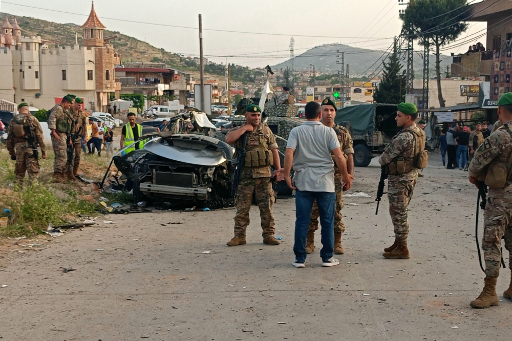 Lebanese army soldiers and onlookers gather around the carcasses of a car after it was hit by an Israeli strike, reportedly killing a local Hamas official, in Majd al-Jabal in Lebanon's Bekaa valley, on May 17, 2024. — AFP pic