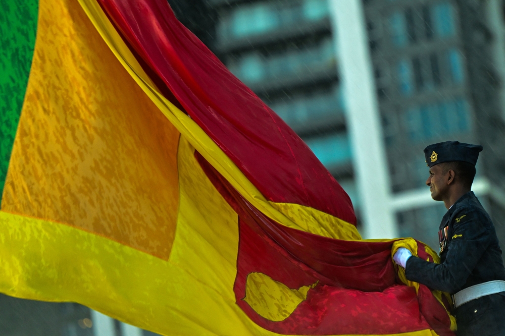 A Sri Lankan soldier lowers the national flag as part of a daily ritual amid rainfall at the Galle Face Green promenade in Colombo on May 14, 2024. — AFP pic