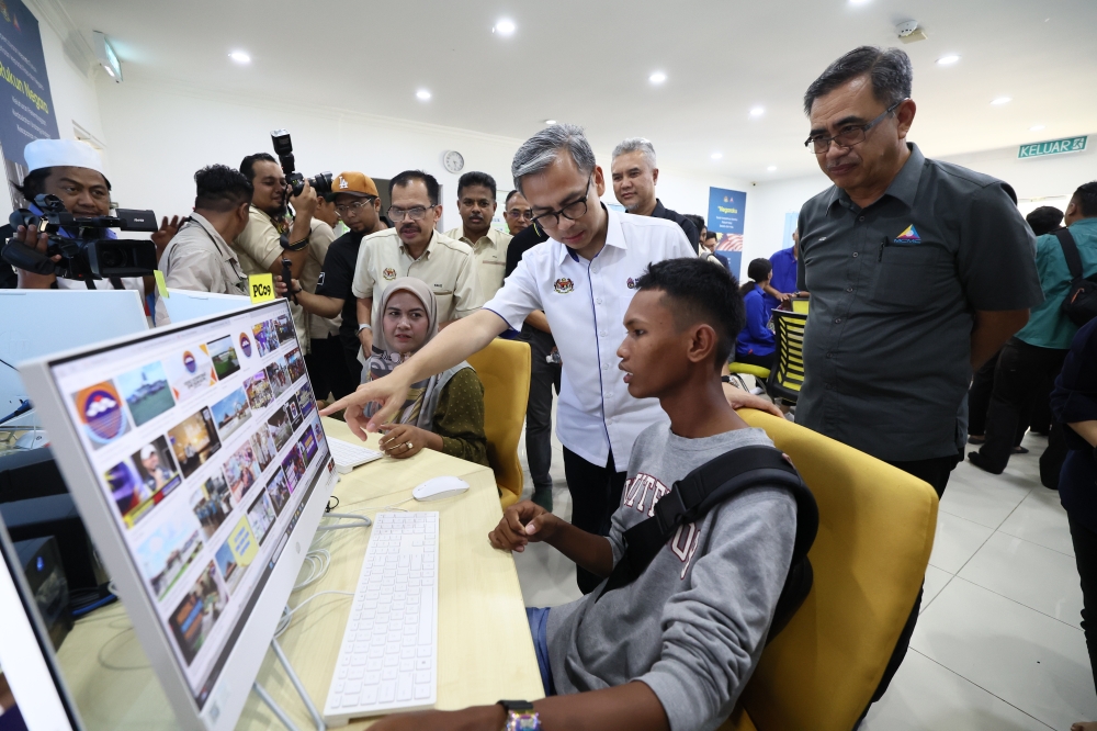 Communications Minister Fahmi Fadzil (2nd right) and Irfan Hamizan Mohd Razli (right) look at computer and internet facilities at the National Information Dissemination Centre (Nadi) in Kampung Terusan Tengah, Pulau Bum Bum May 18, 2024. — Bernama pic