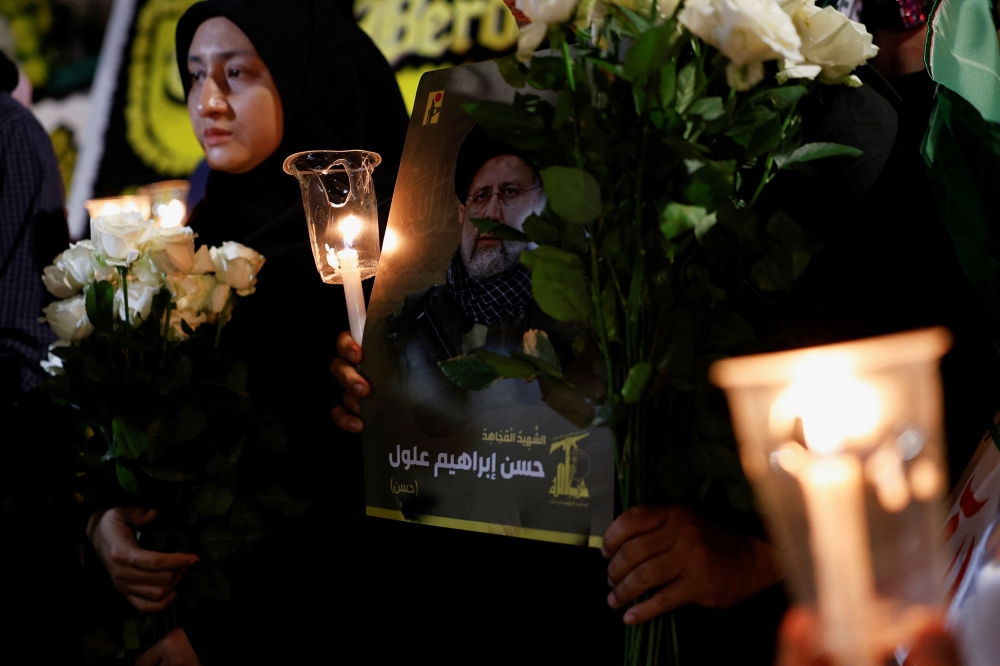 People holding flowers, candles, and a picture of the late Iranian President Ebrahim Raisi, attend a vigil to pay tribute to him and other victims who died in a helicopter crash,  outside the Iranian embassy in Jakarta, Indonesia, May 20, 2024. — Reuters pic