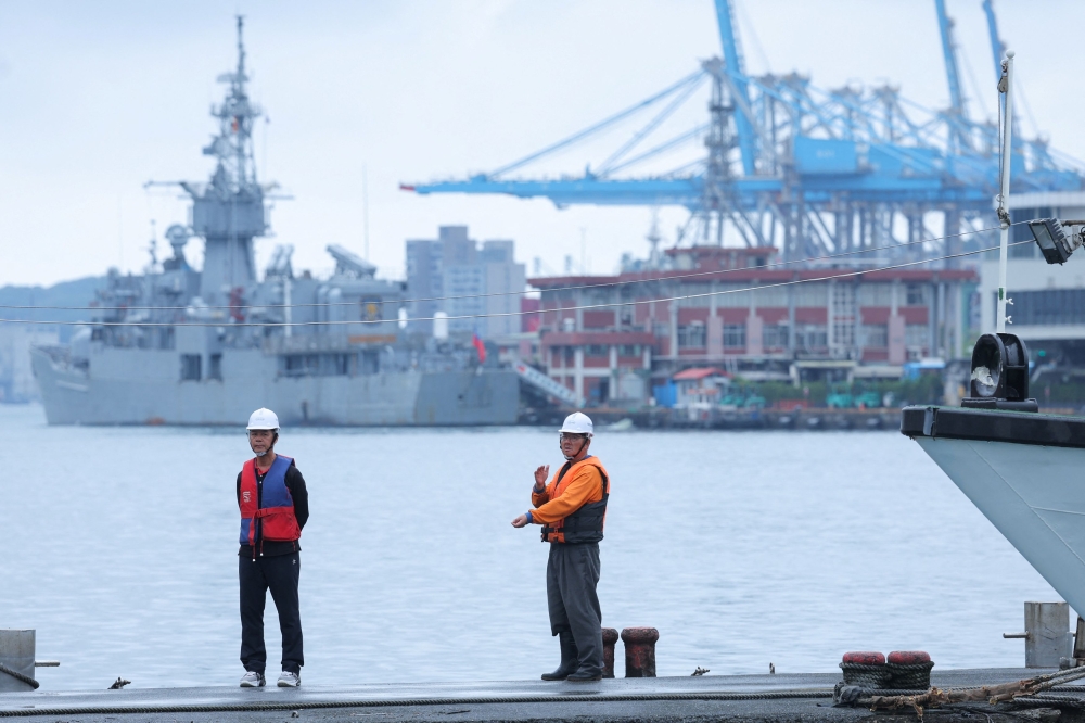 Two staff members look on as navy ships park at the port in Keelung, Taiwan as China announces new military drills around the island today. — Reuters pic