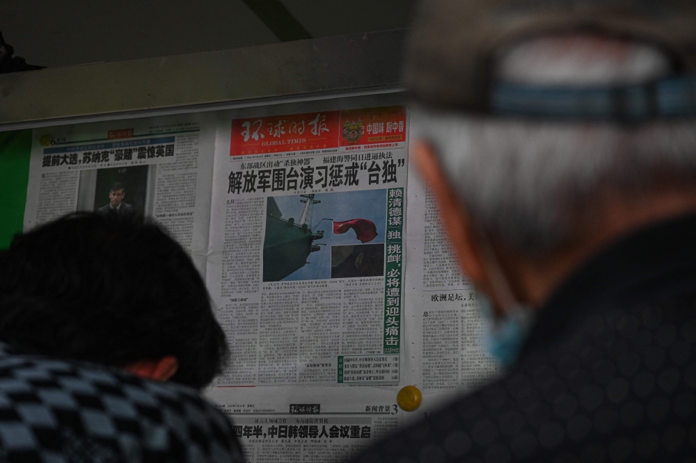 People read a Chinese newspaper with news coverage of China military drills around Taiwan, in Beijing May 24, 2024. — AFP pic
