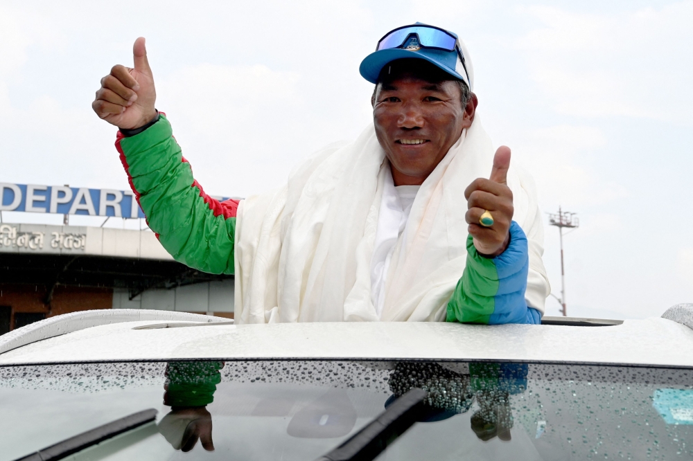 Nepali mountaineer Kami Rita Sherpa, who broke his own record for scaling Mount Everest for the 30th time, gestures to the crowd upon his arrival at the Tribhuvan International airport in Kathmandu May 24, 2024. — AFP pic