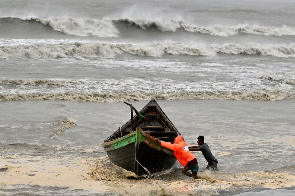 Men pushing a fishing boat to the shore as a preventive measure in Kuakata ahead of cyclone Remal’s landfall in Bangladesh. — AFP pic