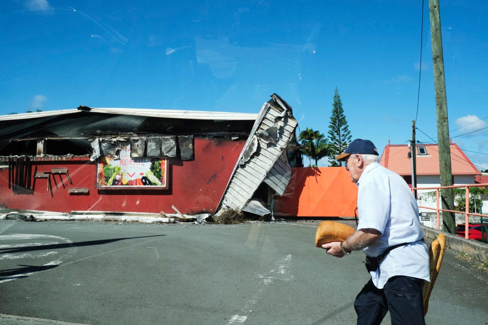 A man walks past a damaged supermarket in Noumea. — AFP pic