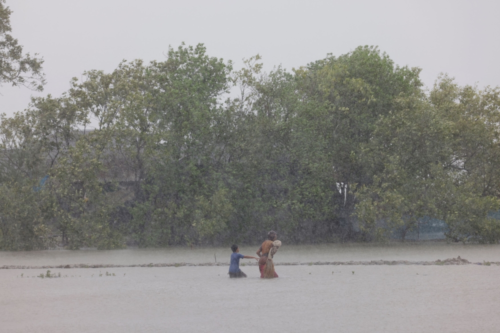A woman and child wade through water as Cyclone Remal hits the country, in the Shyamnagar area of Satkhira, Bangladesh May 27, 2024. ― Reuters pic
