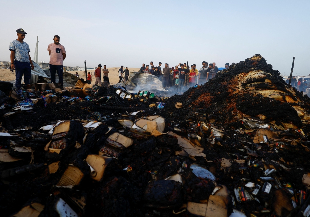 Palestinians look at the damages while searching for food among burnt debris at the site of an Israeli strike on an area designated for displaced people, in Rafah in the southern Gaza Strip, May 27, 2024. — Reuters pic