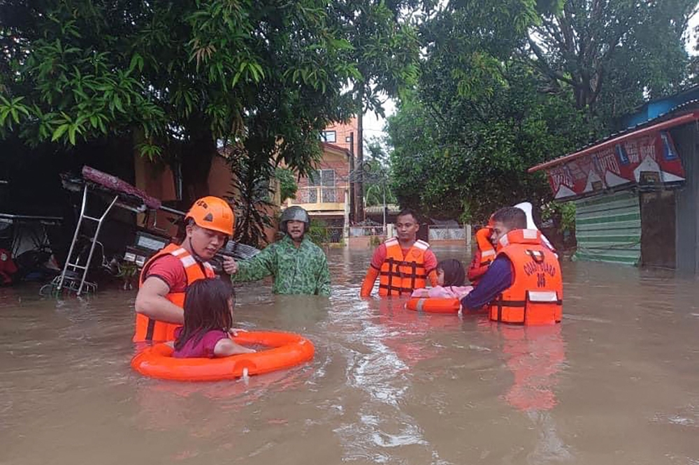 Children are evacuated from a flooded area by coast guard personnel in Lucena, Quezon Province. — AFP pic/Philippine Coast Guard