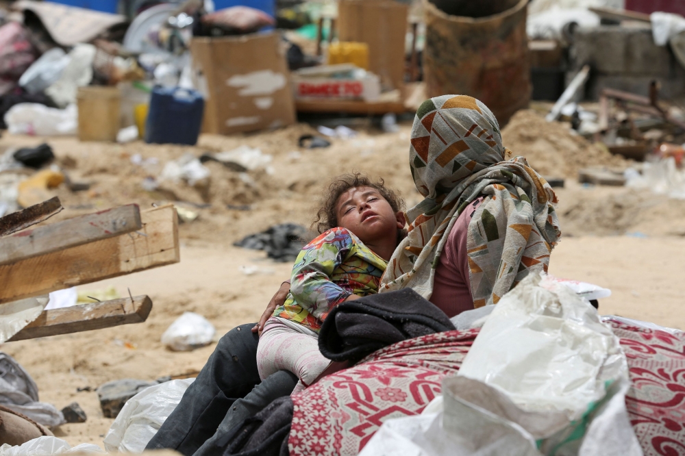 A Palestinian mother rests as the family travelled on foot along with their belongings to flee Rafah due to an Israeli military operation. — Reuters pic